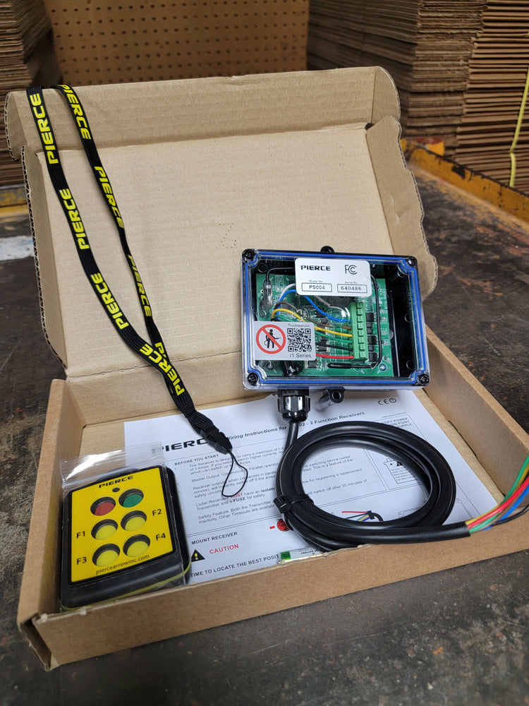 An open box shows the PIERCE 4 Function Wireless Remote Control System with electronic components, a remote control, and a lanyard. The instruction manual on the table ensures easy setup for your 12/24V equipment with a strong IP rating.