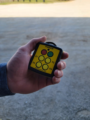 A hand holds the PIERCE 4 Function Wireless Remote Control System, a small device with colored buttons labeled F1 to F4, featuring start and stop controls for 12/24V equipment.