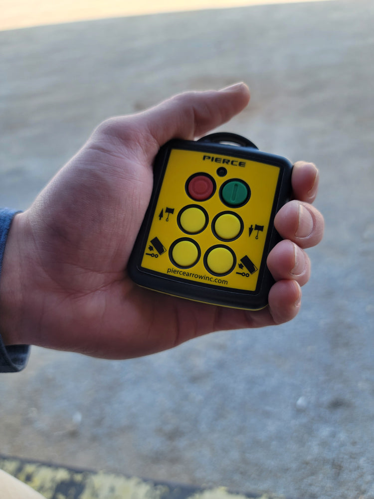 A hand holds a PIERCE 4 Function Wireless Remote Transmitter with a yellow face featuring four circular buttons and directional arrows, ideal as a replacement transmitter.