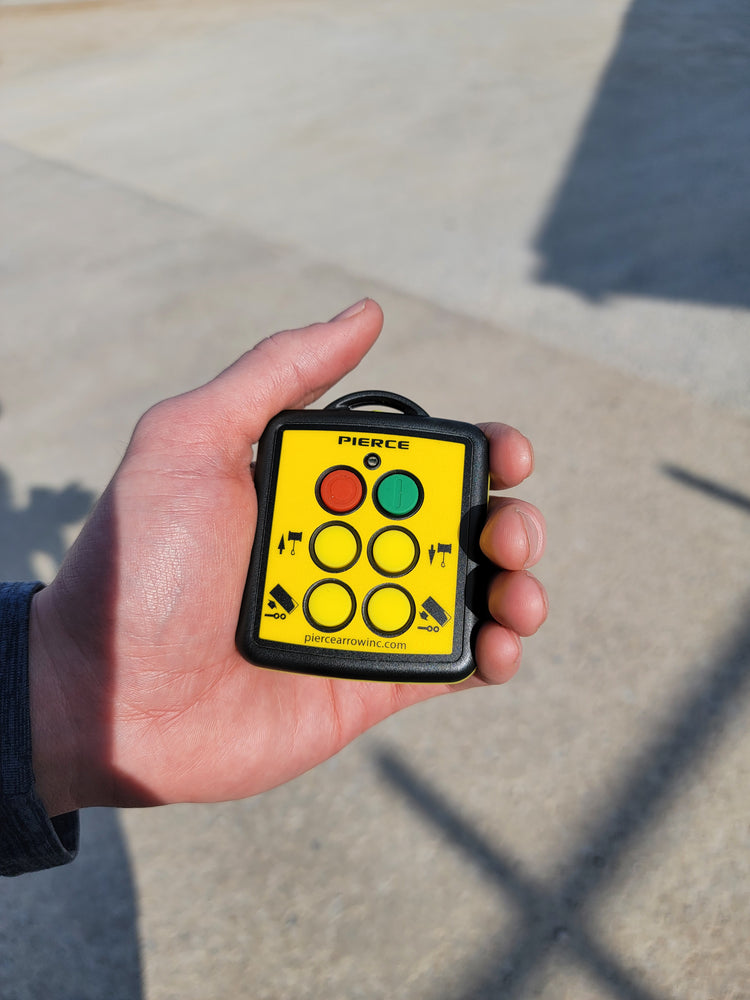 A hand holds a small yellow PIERCE 4 Function Wireless Remote Transmitter with colorful buttons and directional symbols.