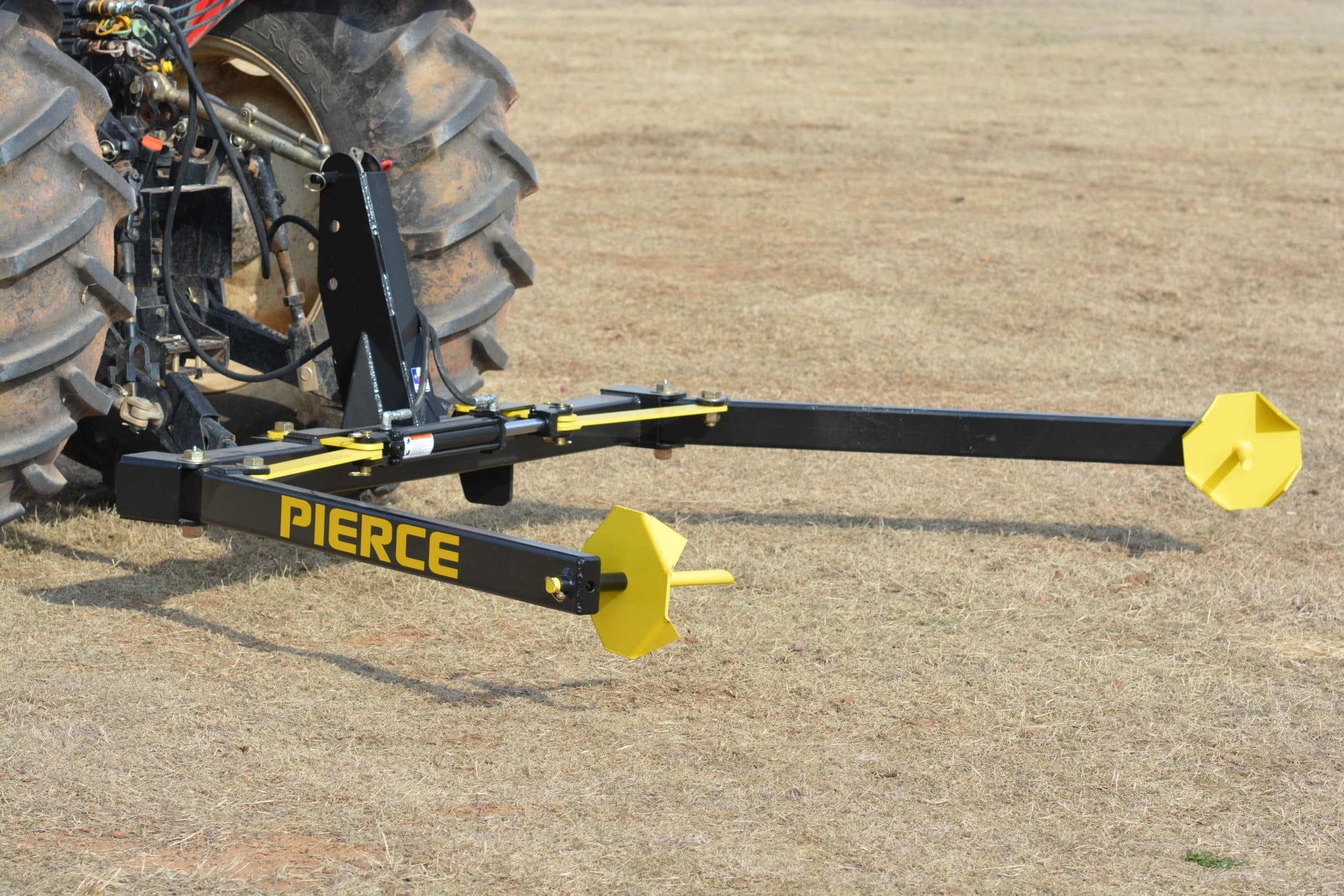 A PIERCE 3-Point Hay Bale Unroller with a yellow and black attachment sits on dry grass, ready to effortlessly tackle large round bales.