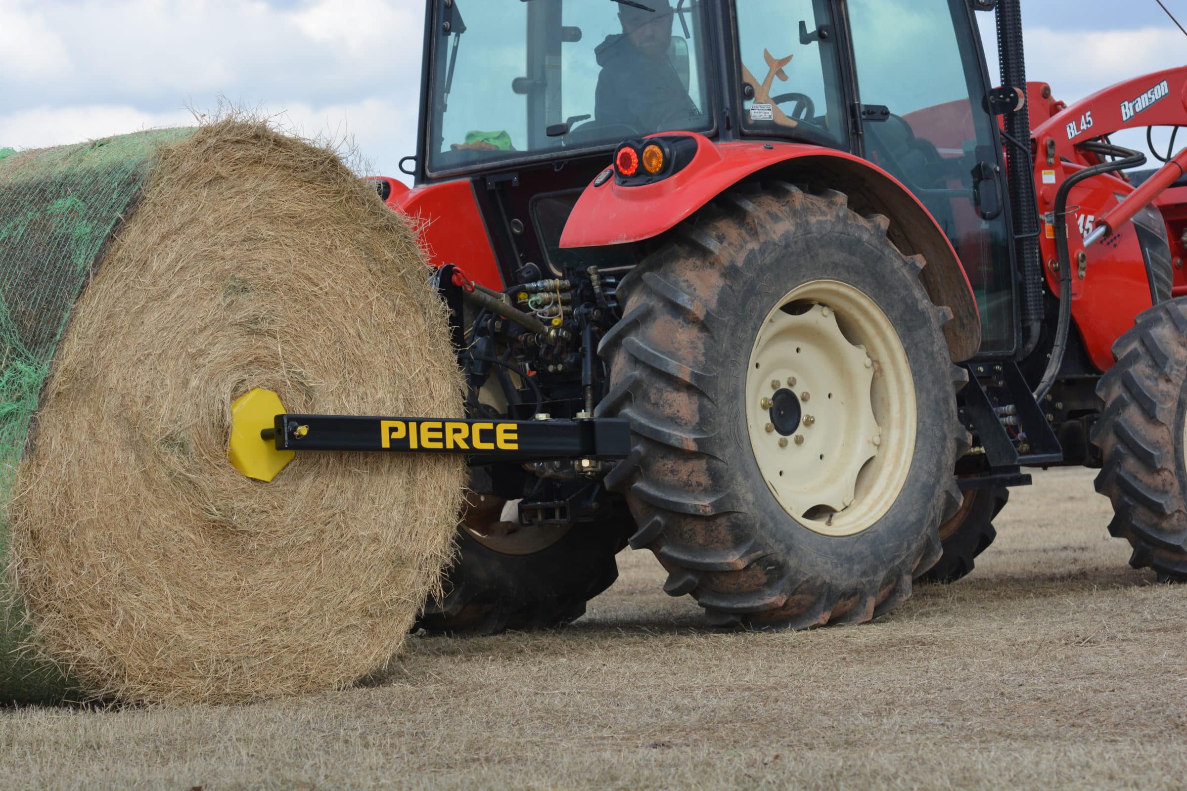 A PIERCE 3-Point Hay Bale Unroller skillfully lifts a large round bale on a grassy field using its specialized forklift attachment.