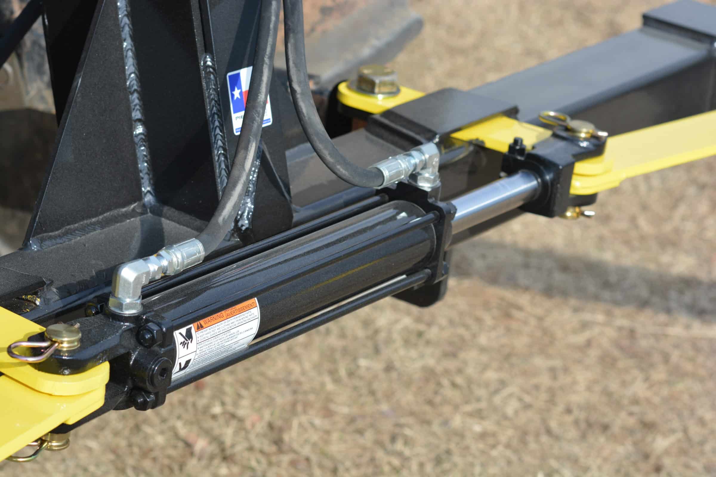 Close-up of a hydraulic cylinder on the 3-Point Hay Bale Unroller by PIERCE, showcasing yellow and black components. This tractor attachment is essential for efficiently managing large round bales.