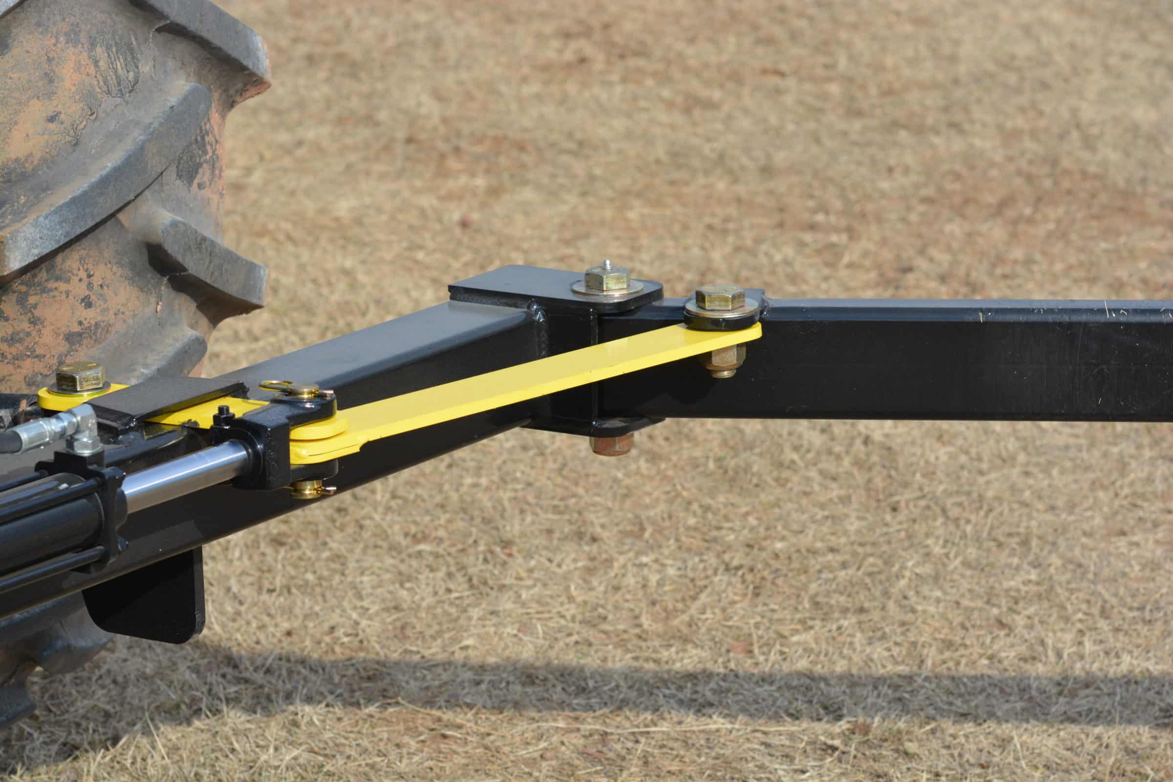 The PIERCE 3-Point Hay Bale Unroller is securely attached to the tractors hitch with bolts, ready for handling large round bales on dry grass.