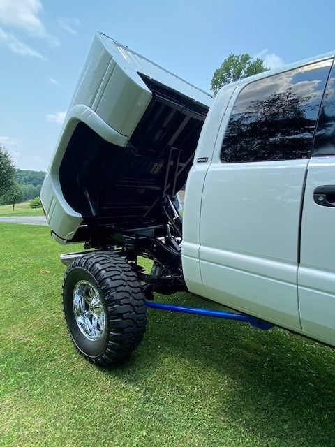 On a grassy field under a clear sky, a lifted truck with an open hood proudly displays its impressive lifting strength, equipped with the PIERCE Factory Bed Dump Kit.